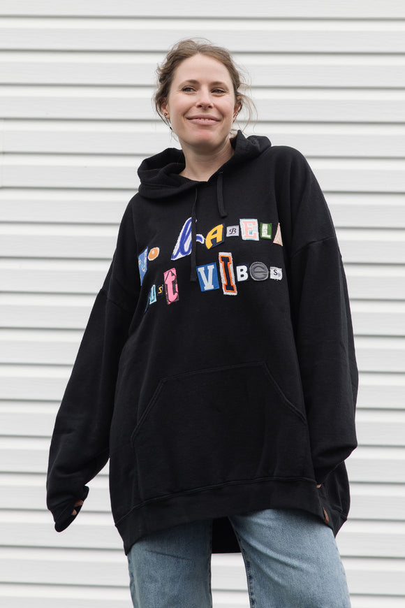 person wearing black hoodie, with random letters spelling 'no labels, just vibes.' upcycled in canada
