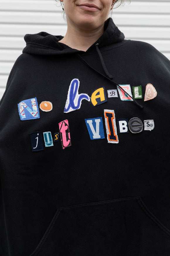 person wearing black hoodie, with random letters spelling 'no labels, just vibes.' upcycled in canada