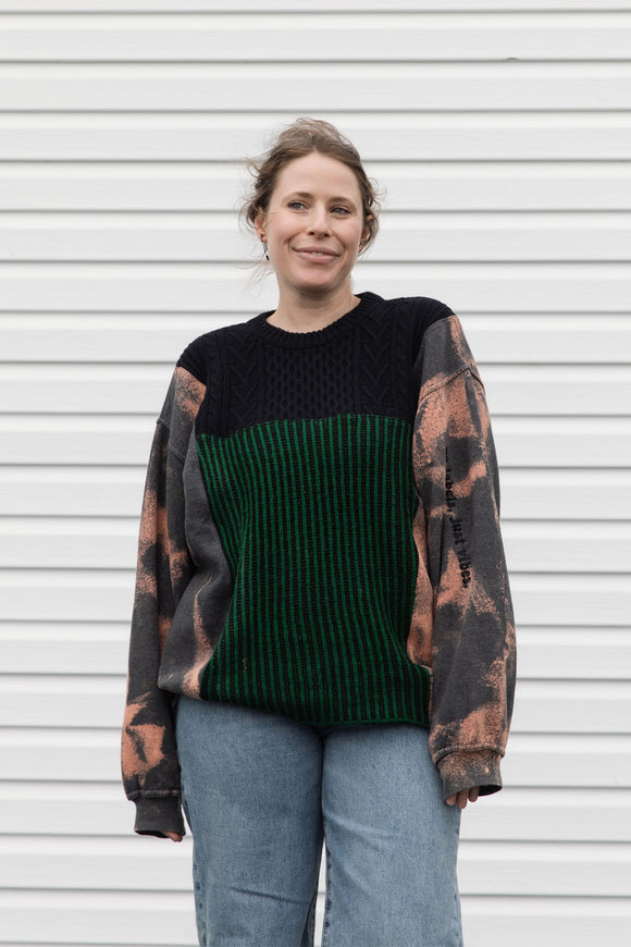 person wearing upcycled sweater with black and green knit and bleached sleeves, featuring 'no labels, just vibes.' embroidered on the sleeve, upcycled in canada