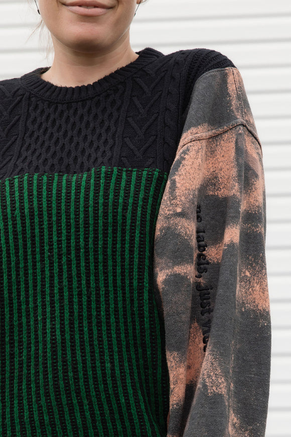 person wearing upcycled sweater with black and green knit and bleached sleeves, featuring 'no labels, just vibes.' embroidered on the sleeve, upcycled in canada