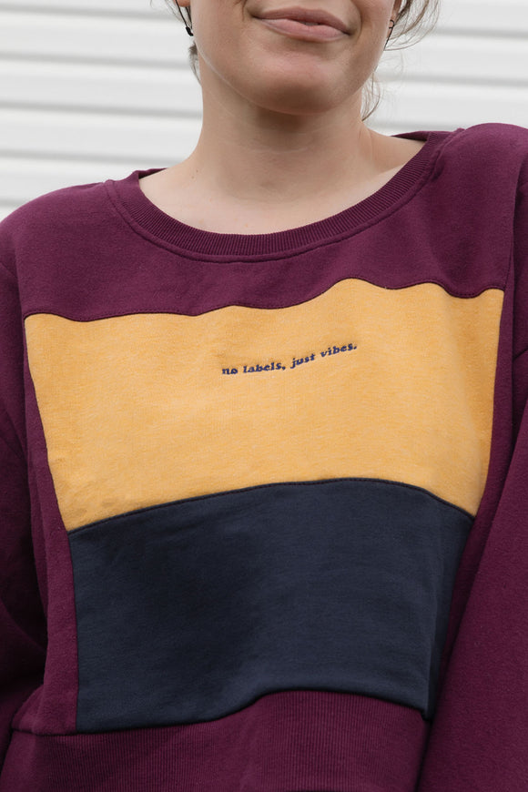 person wearing upcycled sweater, featuring 'no labels, just vibes.' embroidered on the front, repurposed in canada
