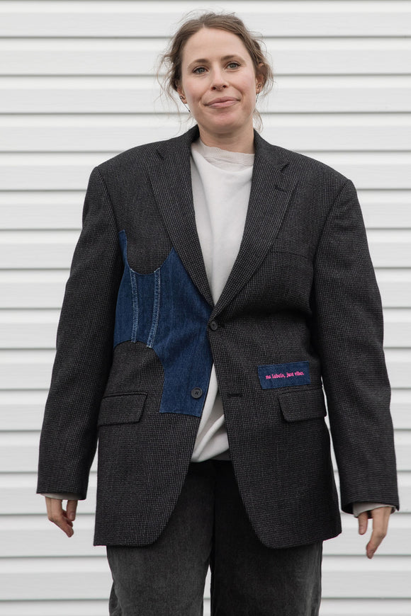 Person wearing a dark gray blazer with denim patch and visible embroidery, upcycled in canada