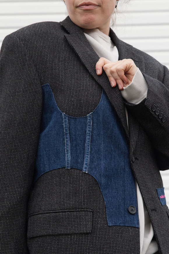 Person wearing a dark gray blazer with denim patch and visible embroidery, upcycled in canada