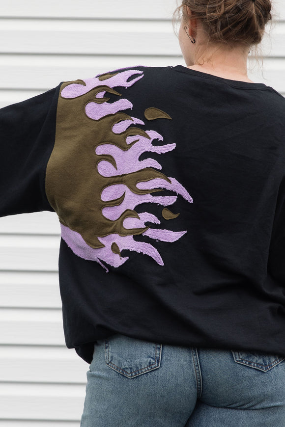 person wearing a black sweater with graphic flames in purple and green, upcycled in canada