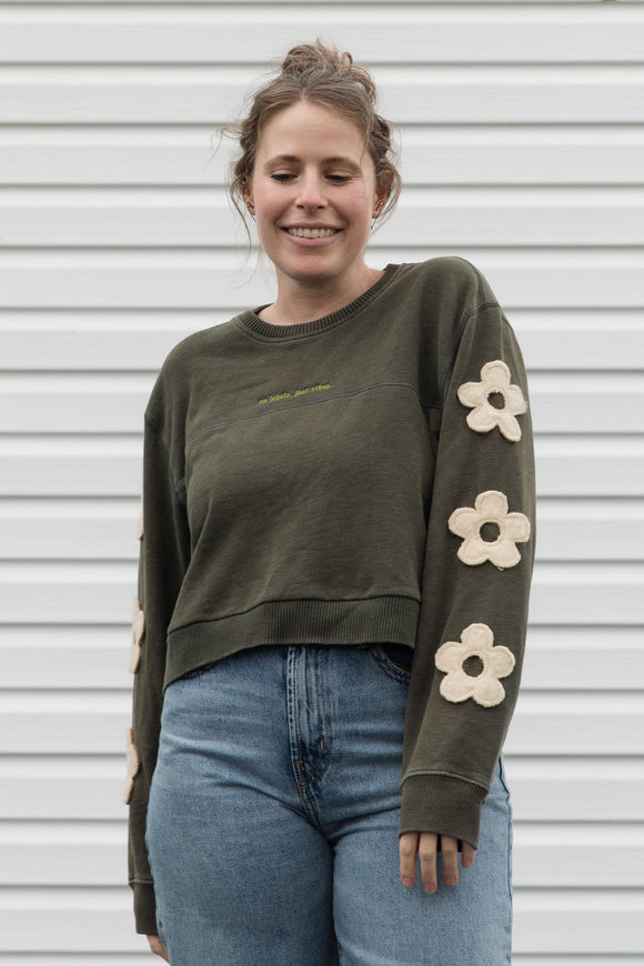 Woman wearing a green sweatshirt with floral designs on sleeves, upcycled in canada