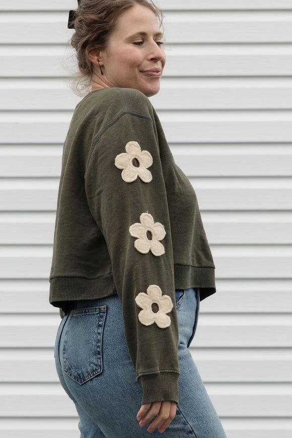 Woman wearing a green sweatshirt with floral designs on sleeves, upcycled in canada