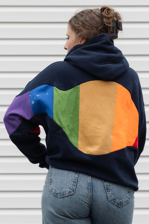 Person wearing a navy hoodie with a colourful rainbow design upcycled in canada