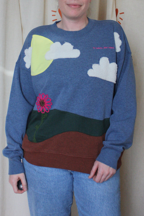 upcycled earth sweater featuring the earth, grass, sky with the sun, clouds and a flower, repurposed in canada
