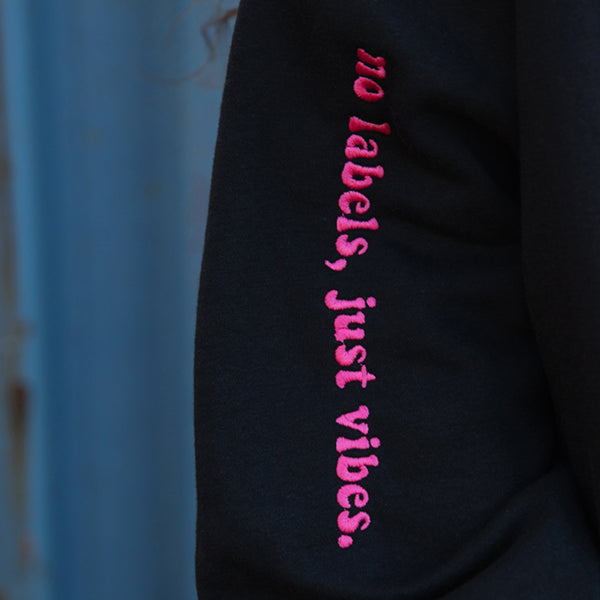 black sweater with 'no labels, just vibes' embroidered in pink thread