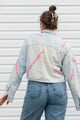A woman viewed from behind wearing a light-wash denim jacket with pink painted line details and blue jeans, standing against a white horizontal-slat wall.