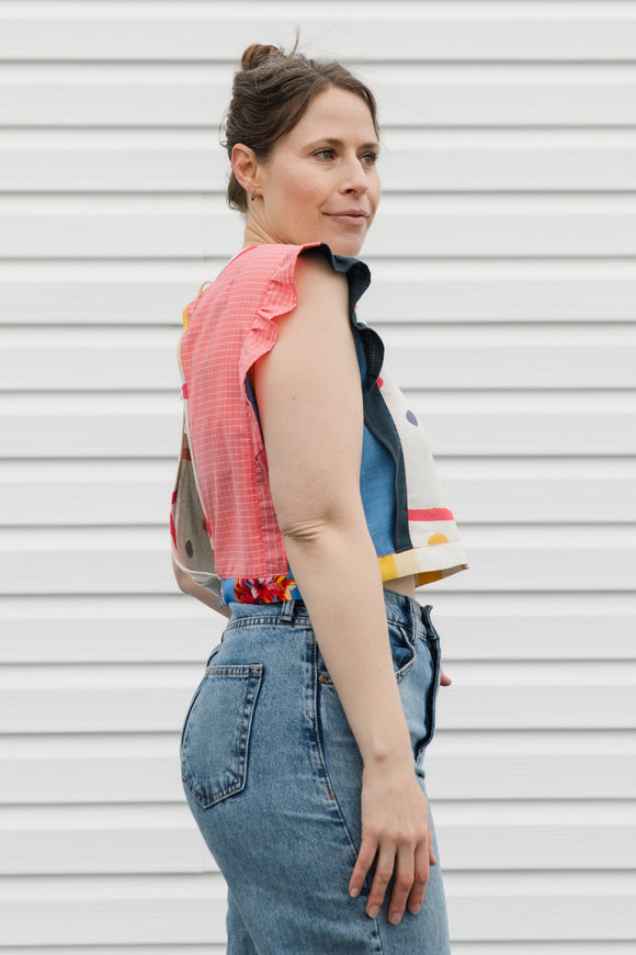 Woman wearing a colorful sleeveless top and denim overalls against a white background