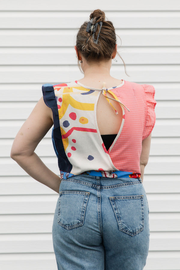 Person wearing a colorful top with a geometric pattern and blue jeans against a white background