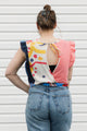 Person wearing a colorful top with a geometric pattern and blue jeans against a white background