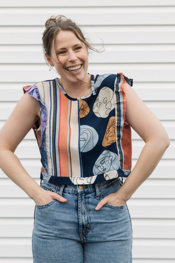 Woman wearing a colorful sleeveless top with minimalist designs against a white wall.