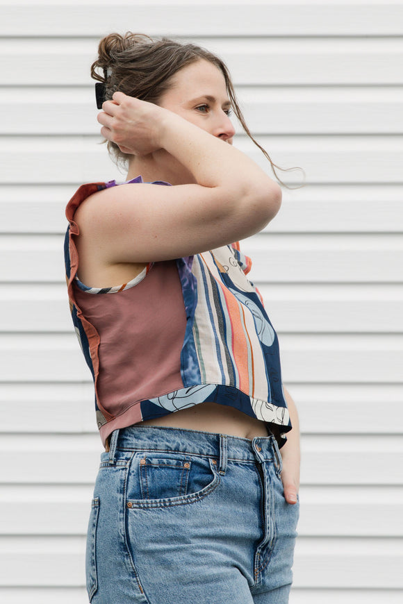 Woman wearing a tank top with a patterned top and jeans against a white wall.