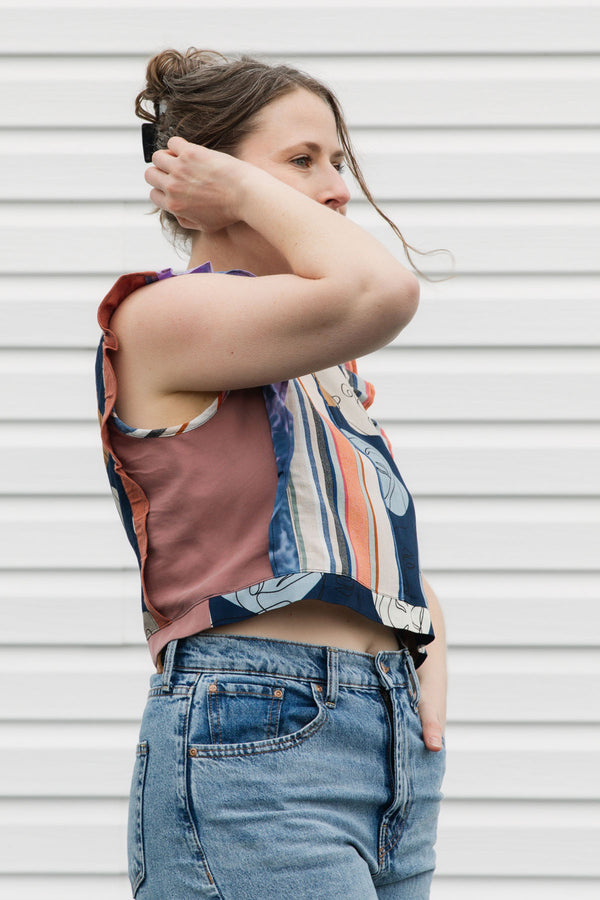 Woman wearing a tank top with a patterned top and jeans against a white wall.