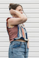 Woman wearing a tank top with a patterned top and jeans against a white wall.