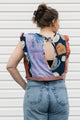 Person wearing a sleeveless top with a unique design and blue jeans against a white background
