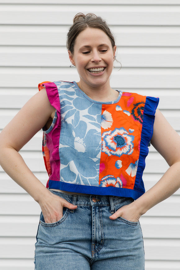 Woman wearing a colorful patchwork top with floral patterns against a plain background