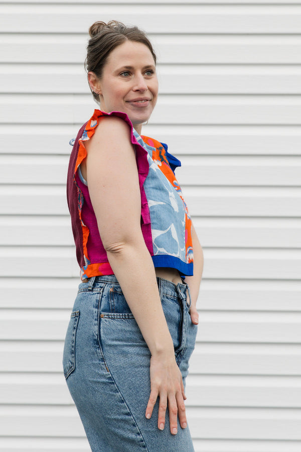Woman wearing a colorful sleeveless top and jeans against a white background