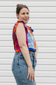 Woman wearing a colorful sleeveless top and jeans against a white background