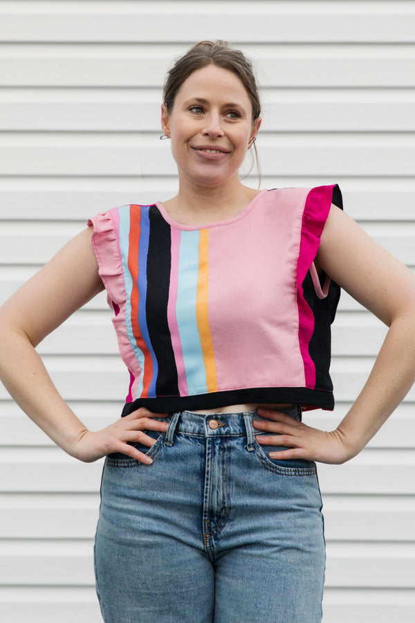 Woman wearing a colorful striped top and jeans against a plain background