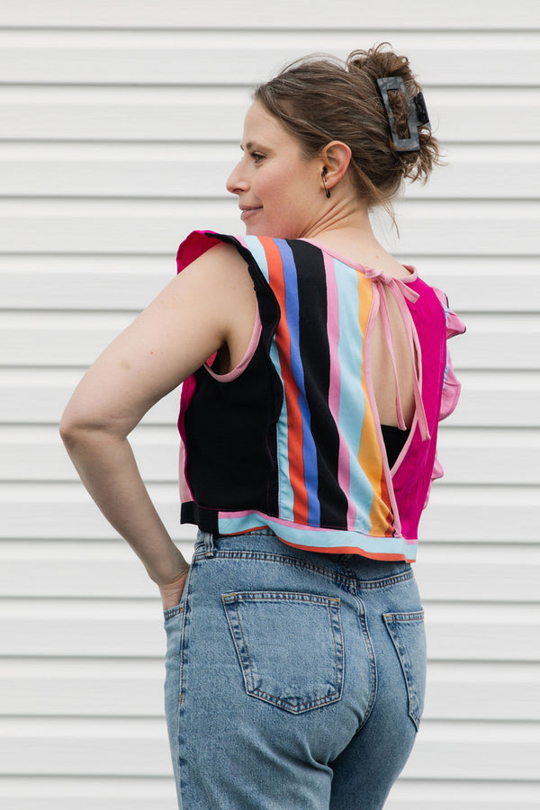Woman wearing a colorful striped top with a pink ribbon and blue jeans against a white background