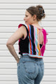 Woman wearing a colorful striped top with a pink ribbon and blue jeans against a white background