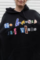 person wearing black hoodie, with random letters spelling 'no labels, just vibes.' upcycled in canada