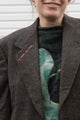 person wearing a brown blazer with floral elbow patches, upcycled in canada. details include no labels, just vibes embroidered on lapel. 