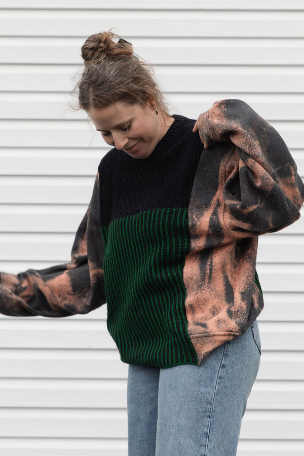 person wearing upcycled sweater with black and green knit and bleached sleeves, featuring 'no labels, just vibes.' embroidered on the sleeve, upcycled in canada