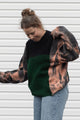 person wearing upcycled sweater with black and green knit and bleached sleeves, featuring 'no labels, just vibes.' embroidered on the sleeve, upcycled in canada