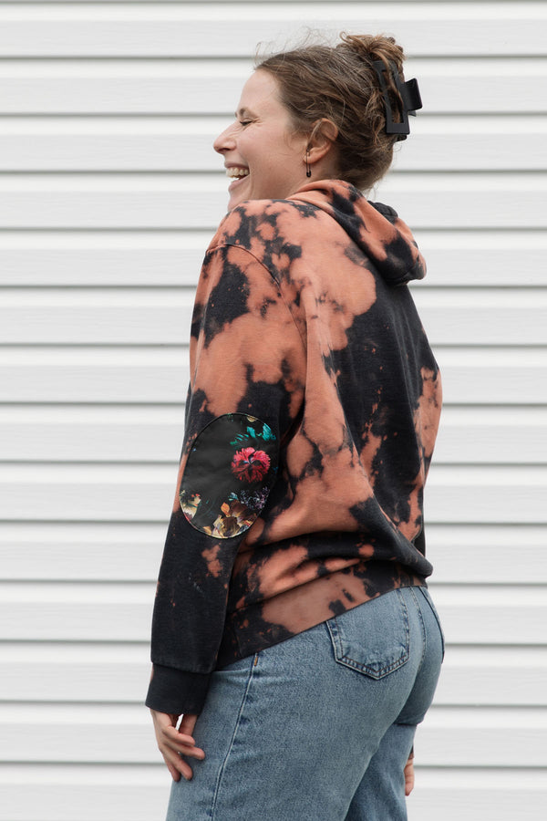 perosn wearing bleached hoodie with floral elbow patches, upcycled in canada