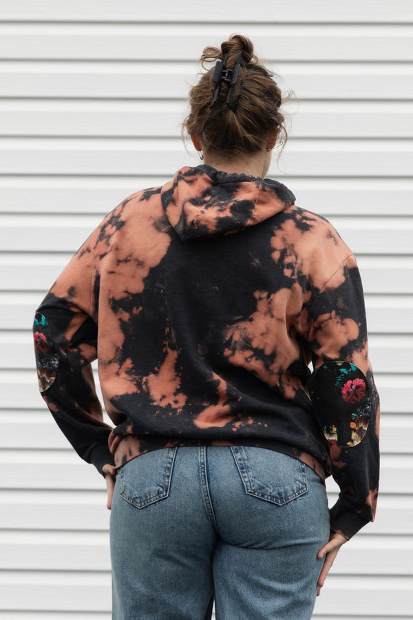 perosn wearing bleached hoodie with floral elbow patches, upcycled in canada