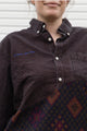 Person wearing a dark brown shirt with a patterned upcycled in canada, details include no labels, just vibes embroidered on shirt