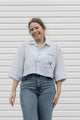 person wearing light blue cropped collared shirt with cow embroidery on breast pocket, upcycled in canada
