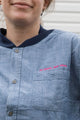 person wearing blue denim button up, upcycled in canada, detail shot featuring 'no labels, just vibes.' embroidery