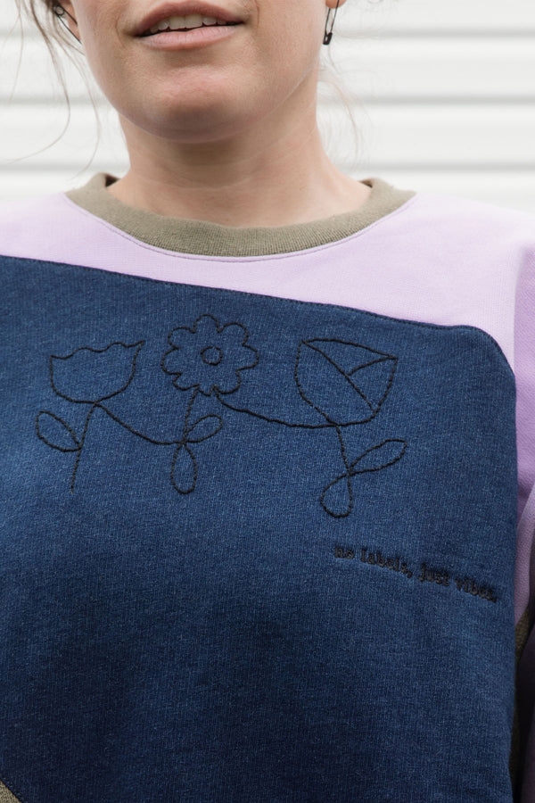Woman wearing a colourful sweater with geometric design, upcycled in canada detail shot of floral hand embroidery