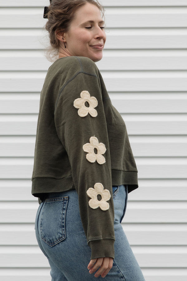 Woman wearing a green sweatshirt with floral designs on sleeves, upcycled in canada