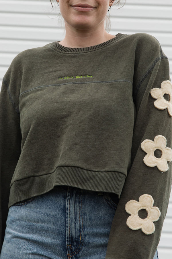 Woman wearing a green sweatshirt with floral designs on sleeves, upcycled in canada detail shot with no labels, just vibes embroidery