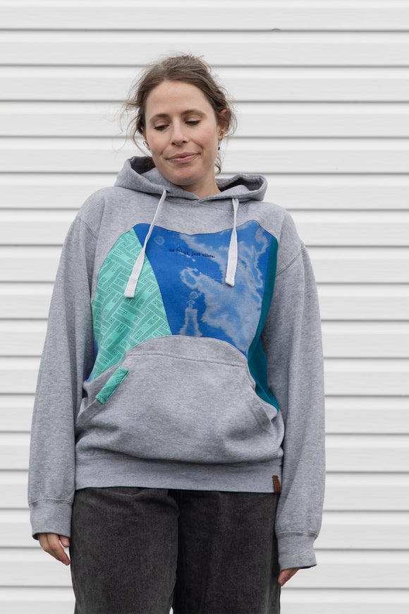 person wearing grey hoodie with blue, teal and green colourful patches, upcycled in canada