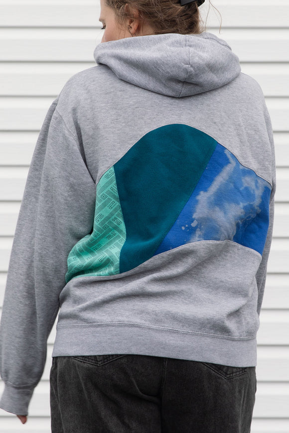 person wearing grey hoodie with blue, teal and green colourful patches, upcycled in canada