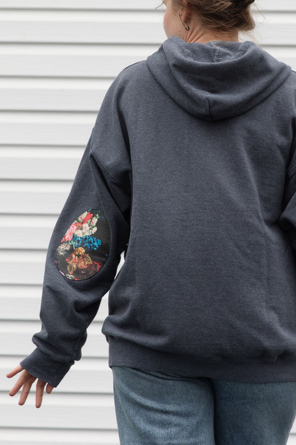 person wearing grey zip up hoodie with floral elbow patches