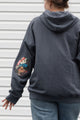 person wearing grey zip up hoodie with floral elbow patches