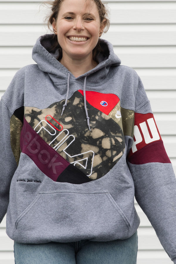 Person wearing a gray hoodie with colorful brand logos, upcycled in canada
