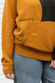 Person wearing a two-tone sweater with mustard yellow and black, upcycled in canada detail shot of 'no labels, just vibes.' embroidery