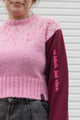 person wearing a pink knit sweater with burgundy sleeves, upcycled in canada, detail shot of 'no labels, just vibes.' embroidery