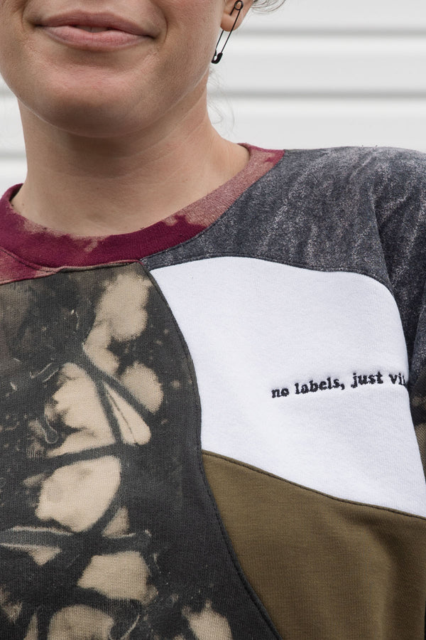 Woman wearing a colorful patterned patchwork sweater upcycled in canada, detail shot of 'no labels, just vibes.' embroidery