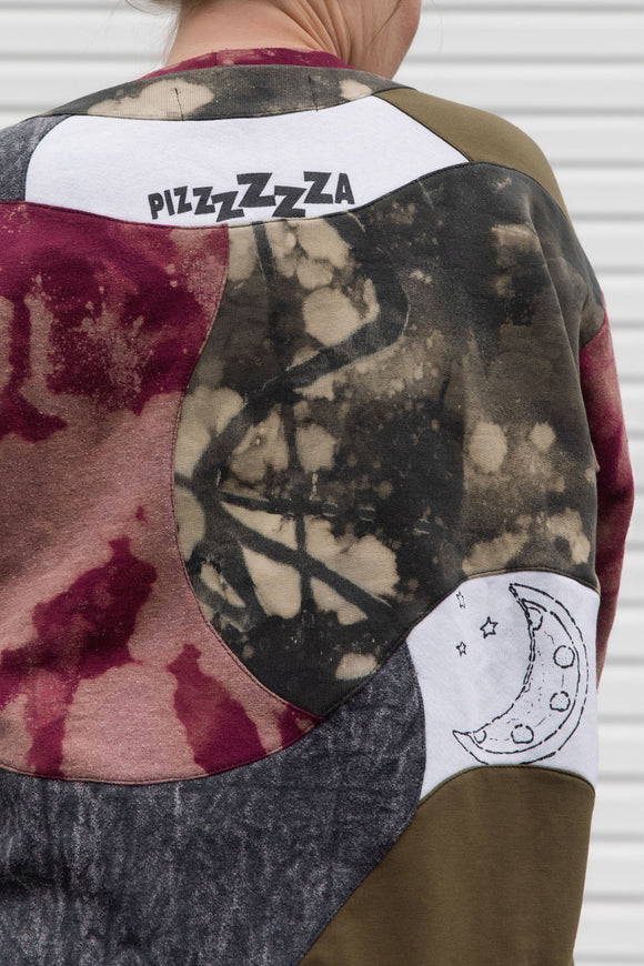 Person wearing a colorful patchwork jacket with 'PIZZZZZA' text on the back, upcycled in canada