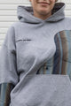 person wearing a grey hoodie with plaid inserts, upcycled in canada, detail shot of 'no labels, just vibes.' embroidery